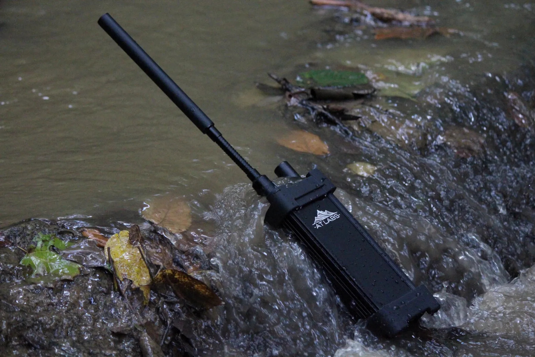 An AT Labs mesh radio standing in fast-moving whitewater, antenna extended, field-tested in a Tennessee creek