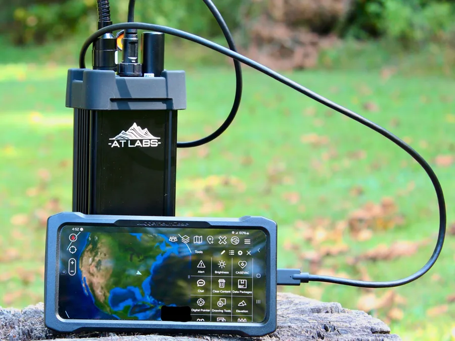 AT Labs RM-1 mesh radio on a stump beside a phone showing the ATAK team map